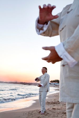 Two older people practicing Taijiquan on the beach at sunset